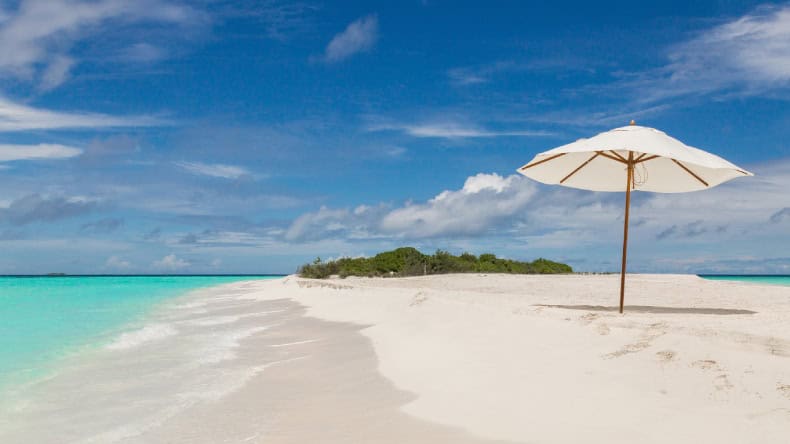 Blick auf eine Sandbank mit weißem Sand, einem Sonnenschirm und Palmen im Hintergrund, Seaside Finolhu Baa Atoll Maldives, Malediven, Indischer Ozean