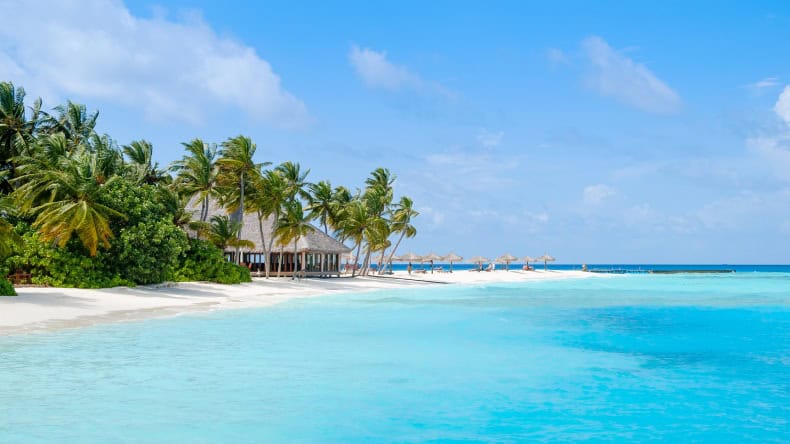 Blick auf einen weißen Sandstrand und eine Sandbank mit Kokospalmen und Sonnenschirmen, Veligandu Maldives Resort Island, Malediven, Indischer Ozean